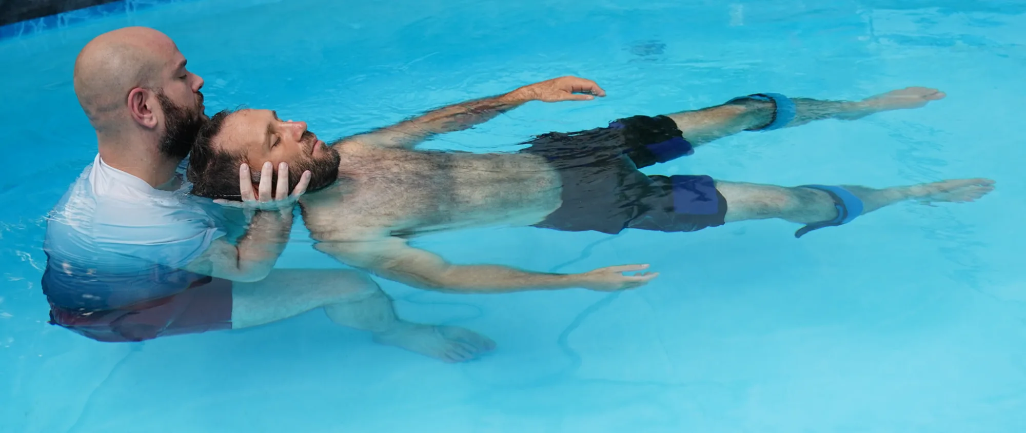 מטפל תומך בראשו של מטופל הצף על גבו במים חמימים במהלך טיפול וואטסו